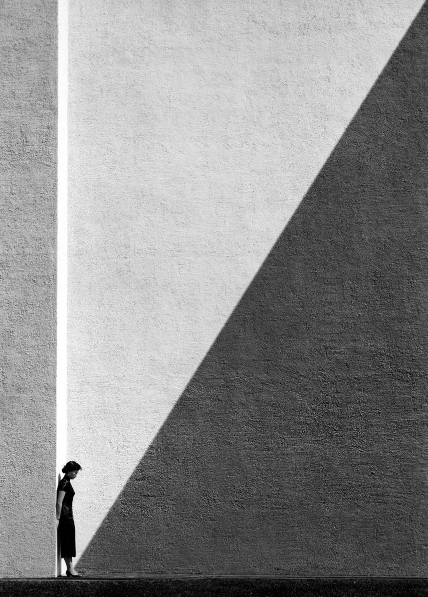 Approaching Shadow, de Fan Ho, 1954 — uma mulher encostada num muro, com uma sombra triangular avançando sobre ela