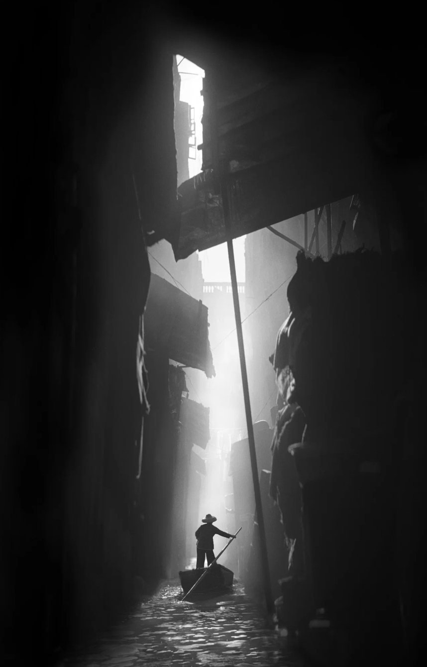 Hong Kong Venice, de Fan Ho, 1962 — um barqueiro em silhueta num beco estreito e escuro, iluminado por um feixe de luz vertical