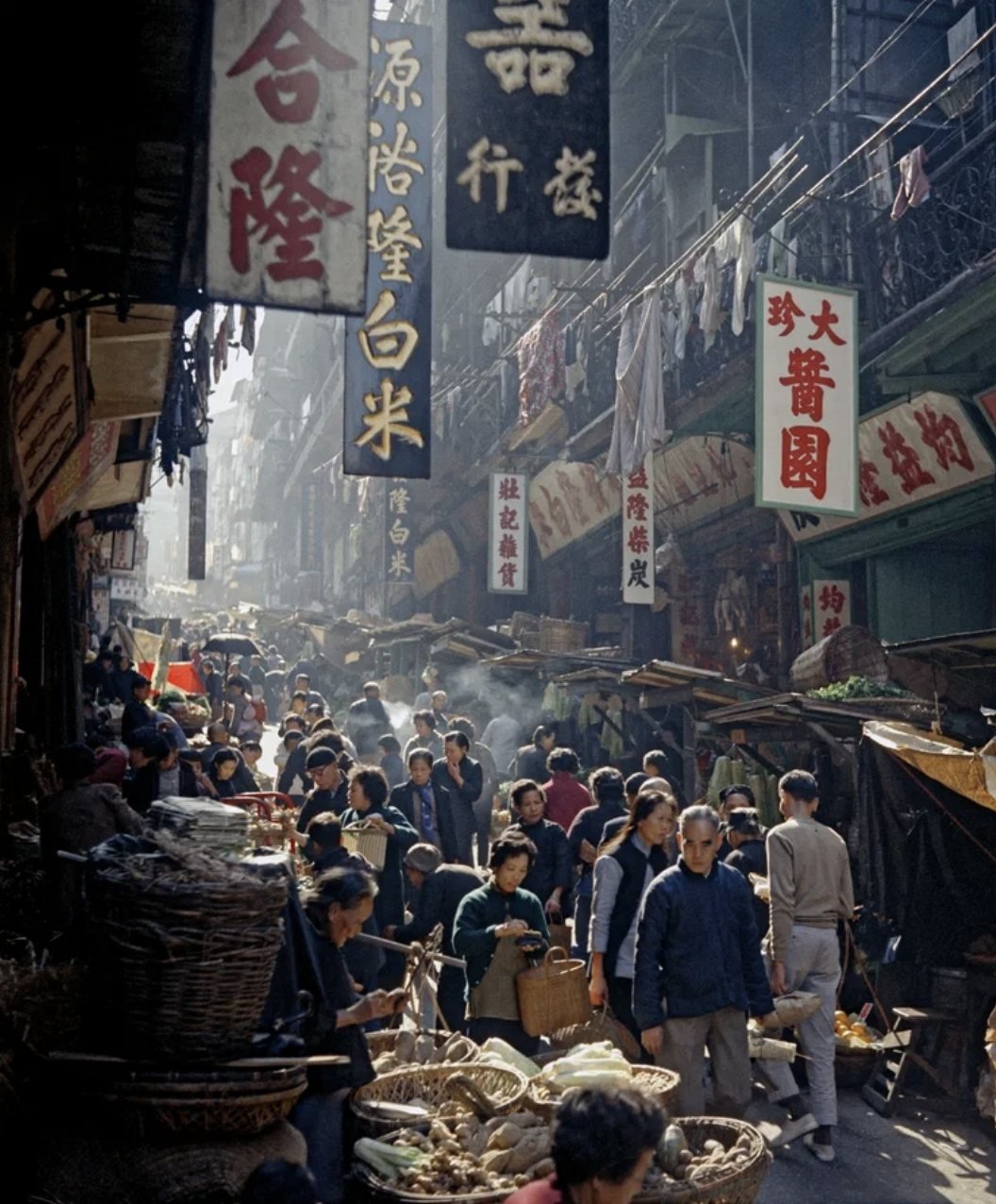 Market Promenade, de Fan Ho — rua de mercado movimentada em Hong Kong, com tabuletas penduradas e vapor no ar