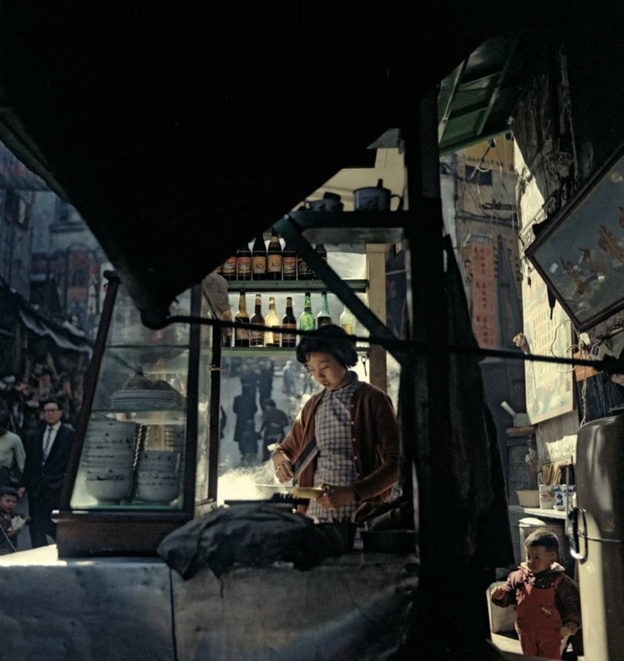 Mom's Second Kitchen, de Fan Ho — uma vendedora prepara comida numa banca de rua em Hong Kong
