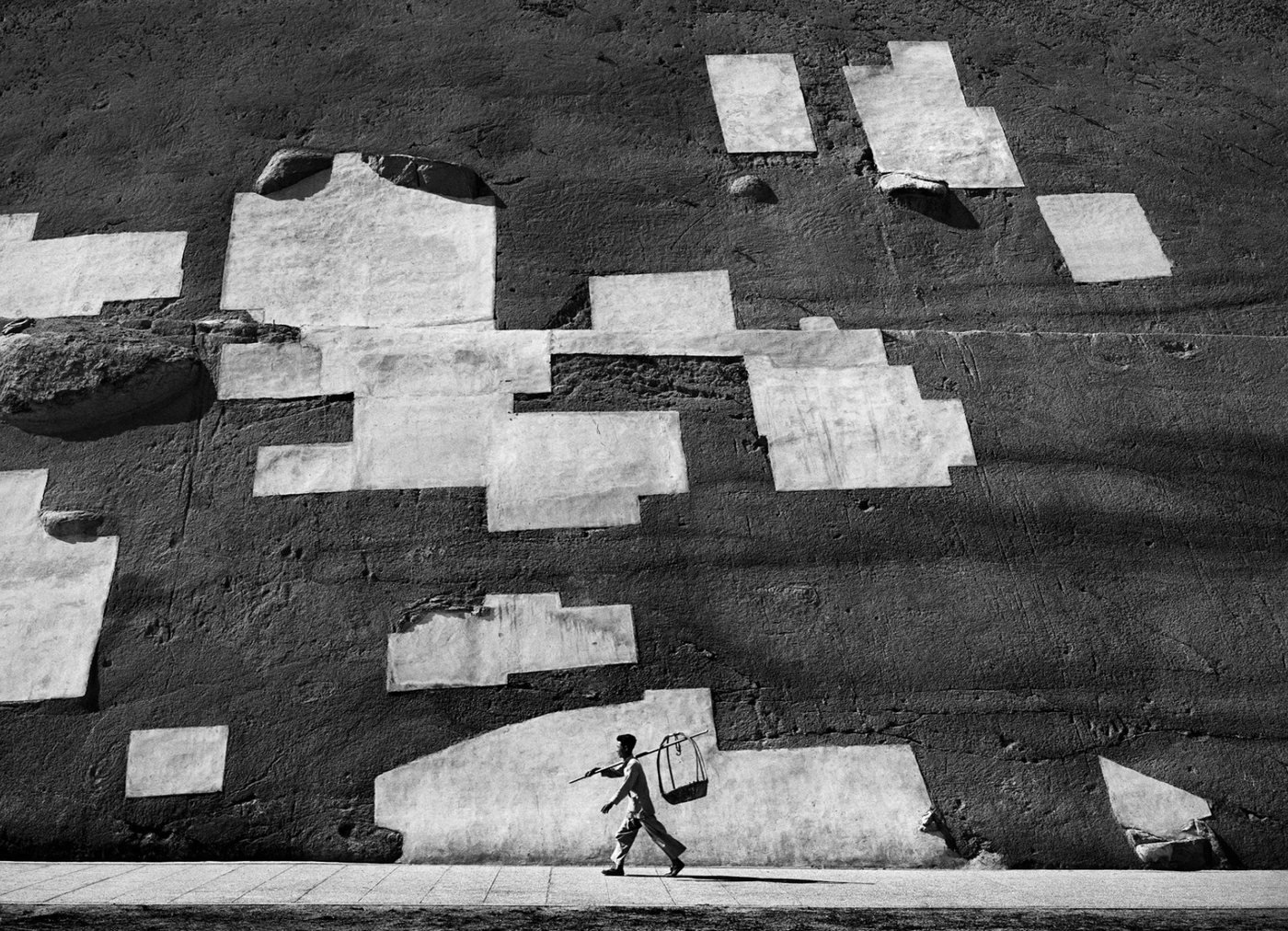 Pattern, de Fan Ho, 1956 — parede com remendos de argamassa formando um padrão gráfico, com um homem passando ao fundo